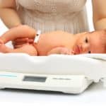 25627688 – mother and her newborn baby on a weight scale over white background